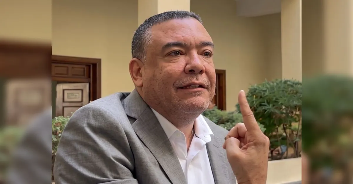 Man in a gray suit and white shirt raises his index finger while speaking outdoors.
