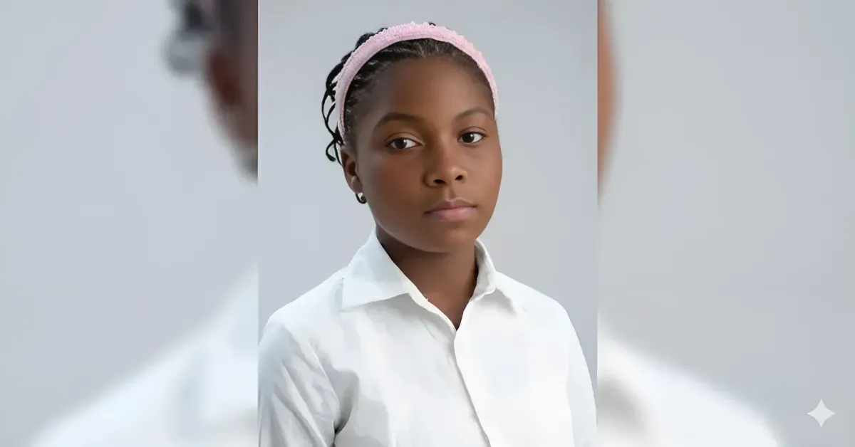 Portrait of a young girl in a white collared shirt with a pink headband, looking at the camera against a light gray background, neutral expression.