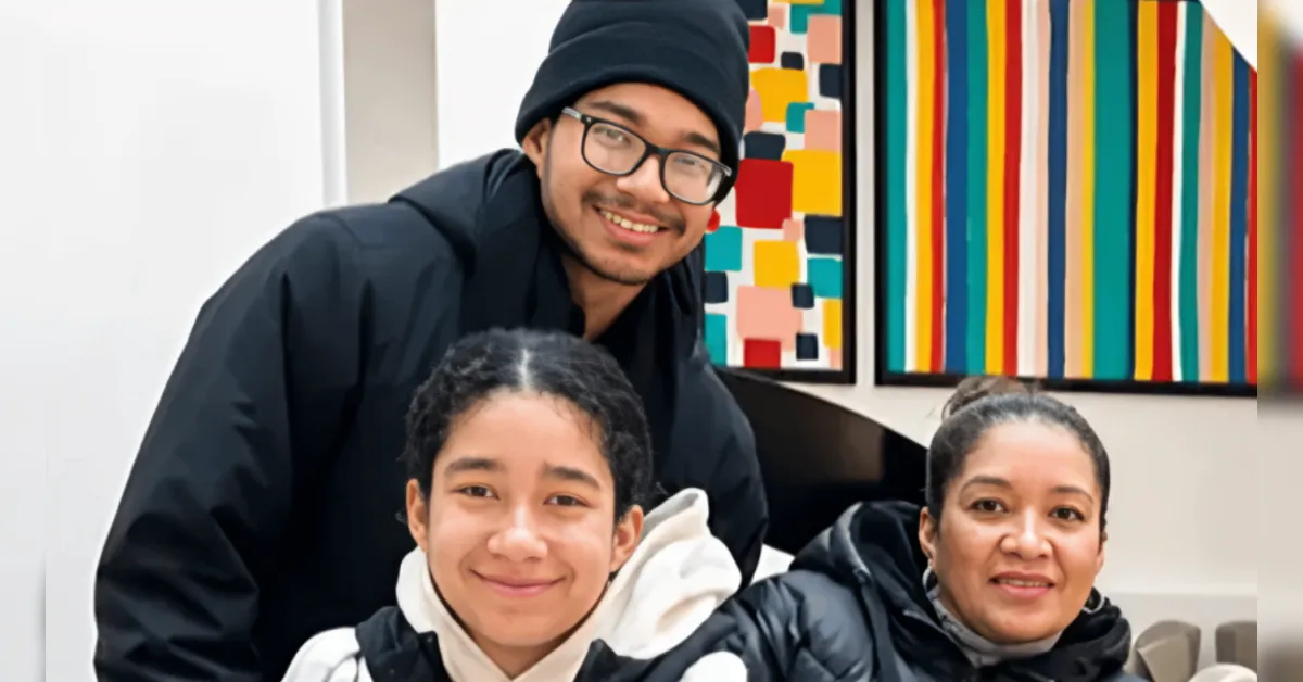 Three people smiling for a photo indoors, with bright abstract paintings on the wall behind them.