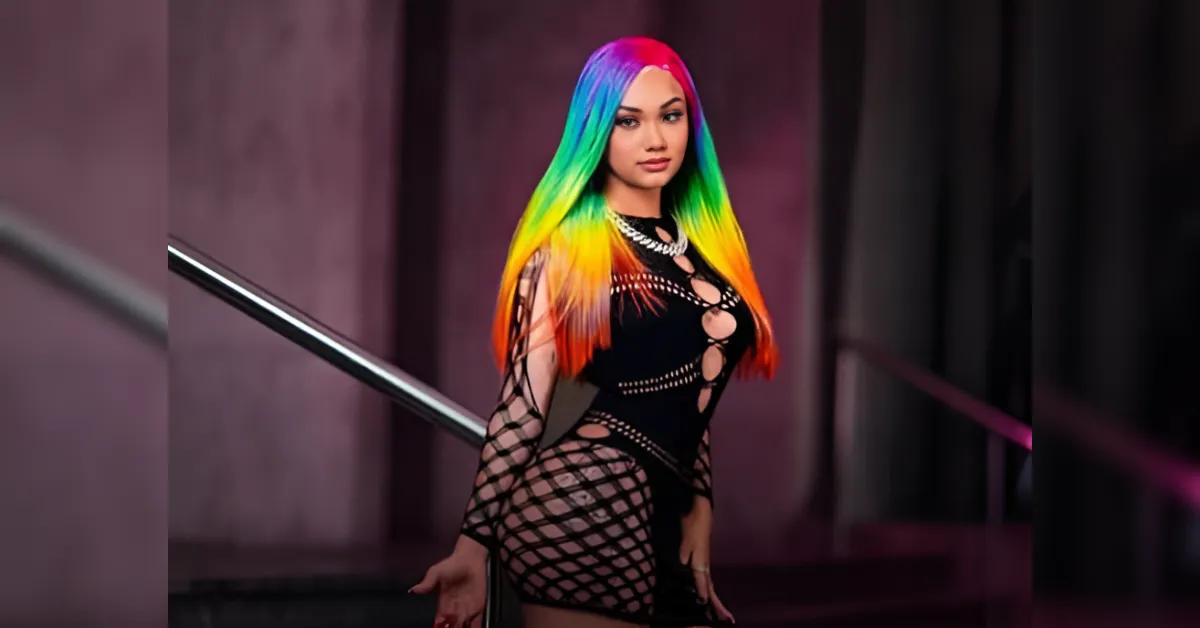Person with rainbow hair wearing a black cut-out outfit posing by a railing.