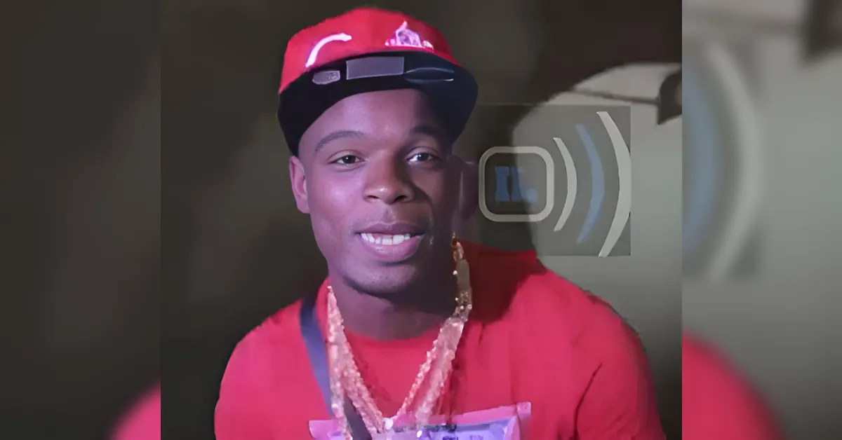 Young man in a red shirt and red cap smiling at the camera, wearing a gold chain necklace.