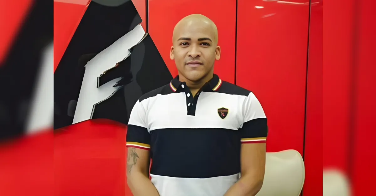 Man with a shaved head wearing a color-block polo shirt stands against red lockers.