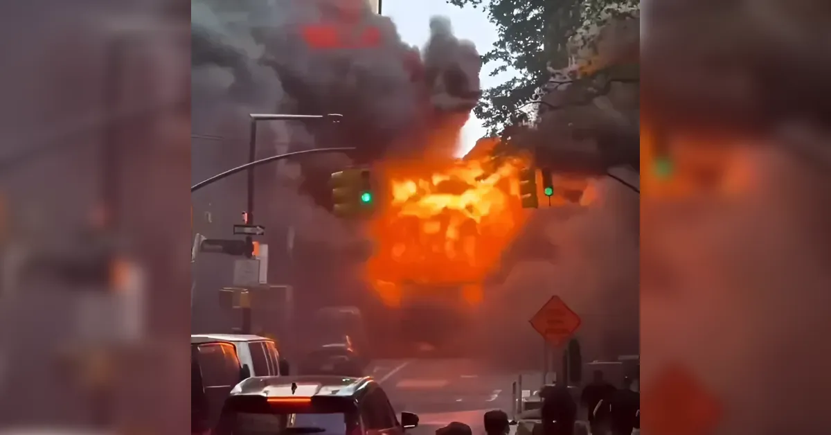 Large explosion on a city street with orange flames and rising smoke, cars in the foreground and bystanders watching.