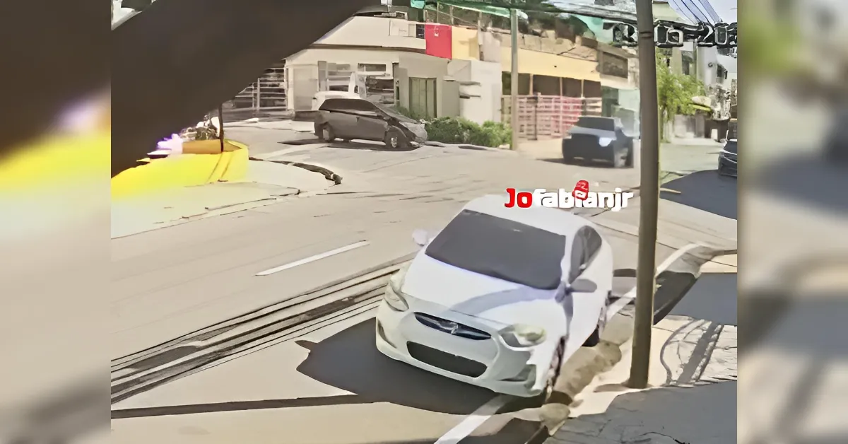 White car parked on a curb beside a utility pole on a sunny urban street; another dark SUV is uphill in the background.