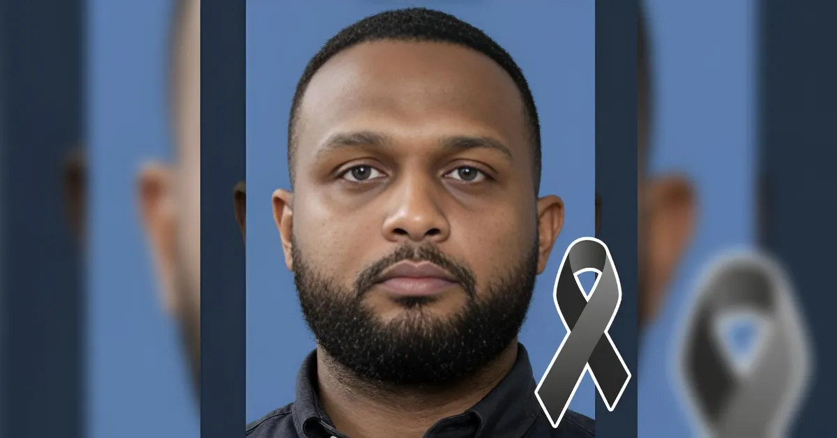Portrait of a man with short hair and beard against a blue backdrop, with a gray awareness ribbon overlay indicating remembrance or support.