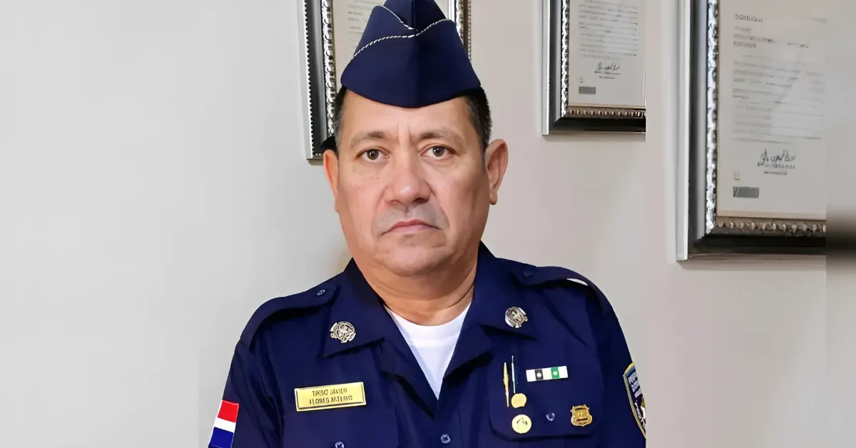Middle-aged officer in dark blue dress uniform with cap, medals, and a flag patch on the sleeve.