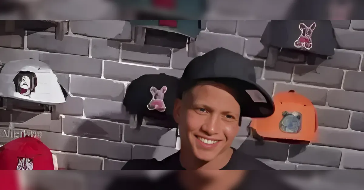 Smiling man wearing a black cowboy hat, posed in front of a wall of hanging hats on a gray brick backdrop.
