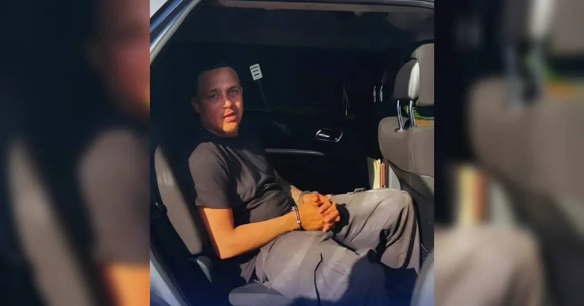 Man sits in the back seat of a car, hands clasped, looking toward the camera.