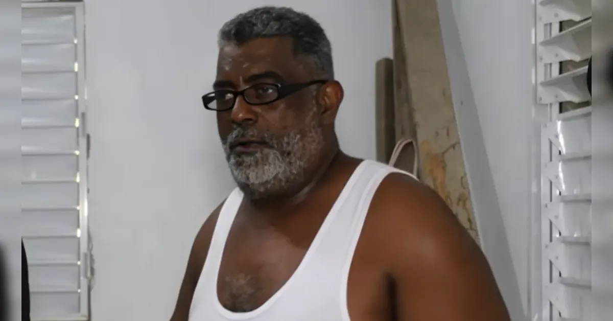 Middle-aged man with salt-and-pepper hair and beard wearing a white tank top and glasses indoors, with dust on his face.