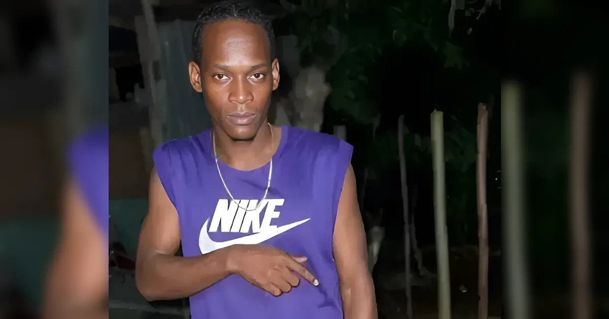 Young man in a purple Nike sleeveless shirt points to his chest during a nighttime outdoor setting.