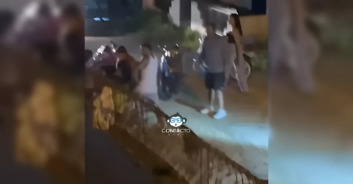 A group of people standing and walking outdoors at night near a railing, with a logo watermark in the center bottom.
