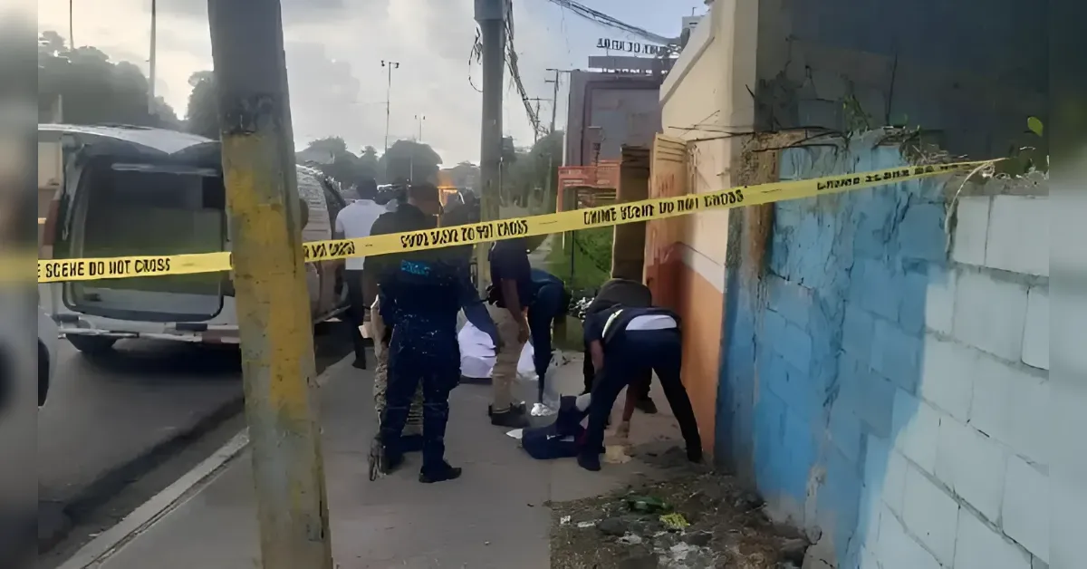 Crime-scene on a sidewalk with yellow Do Not Cross tape, several people gathered around a body covered on the ground near a blue wall and a van.