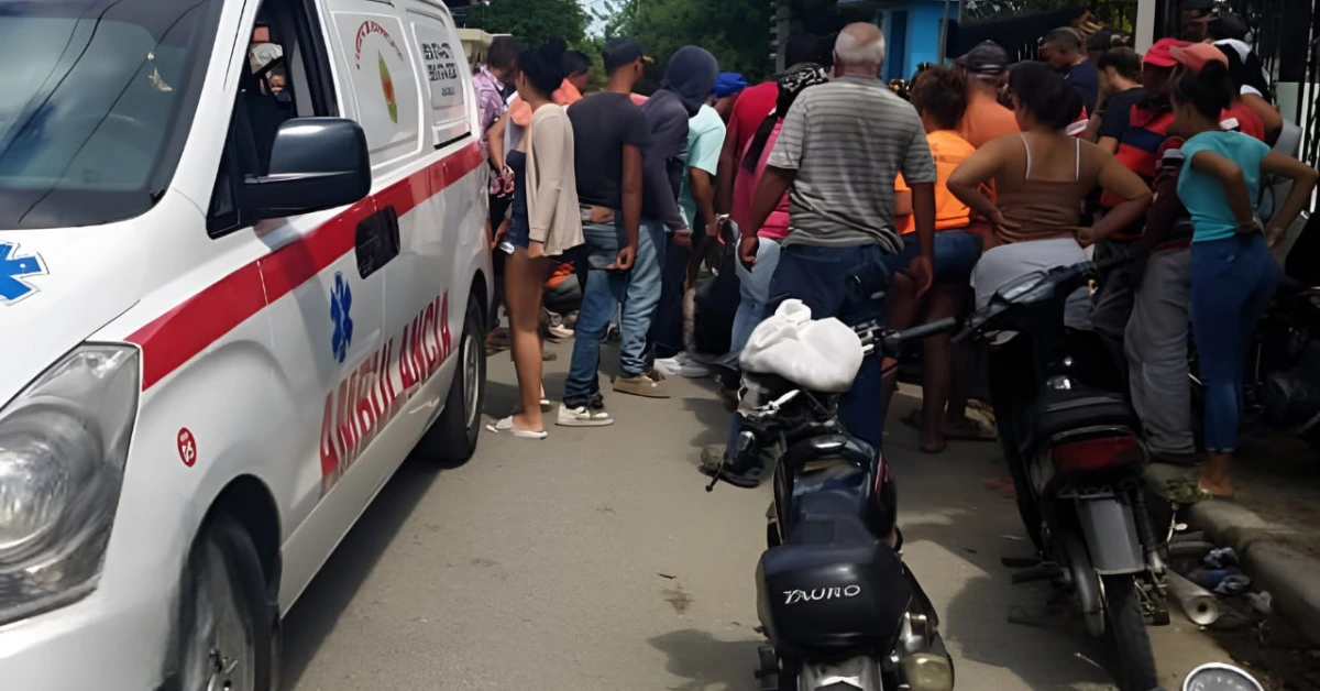 Ambulance parked on a busy street with a crowd of people gathered nearby and motorcycles parked along the curb.
