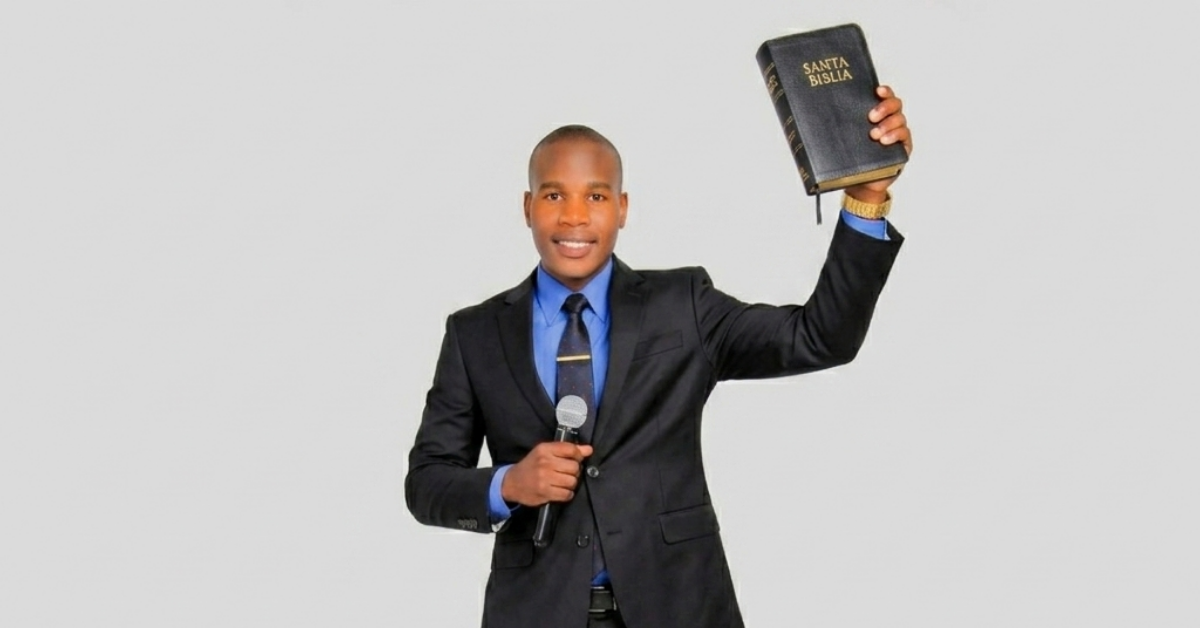 Young man in a dark suit raises a Bible while holding a microphone.