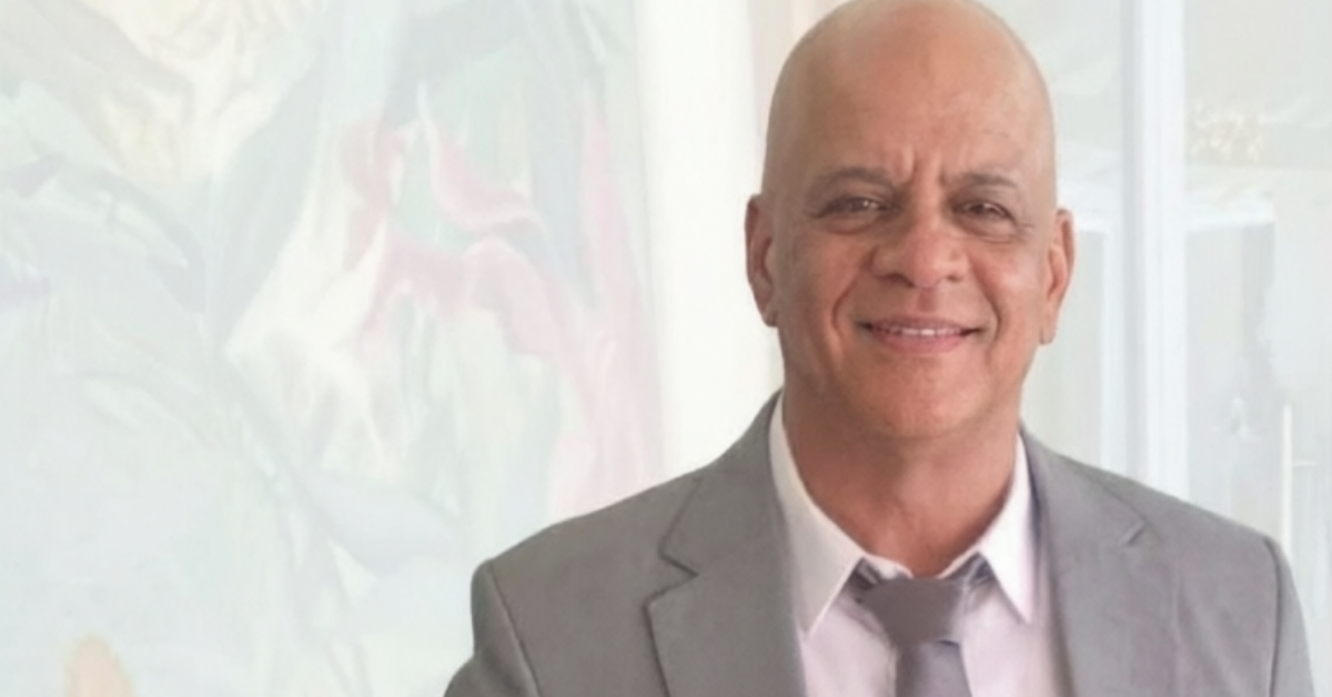 Smiling bald man in a gray suit and tie standing indoors.