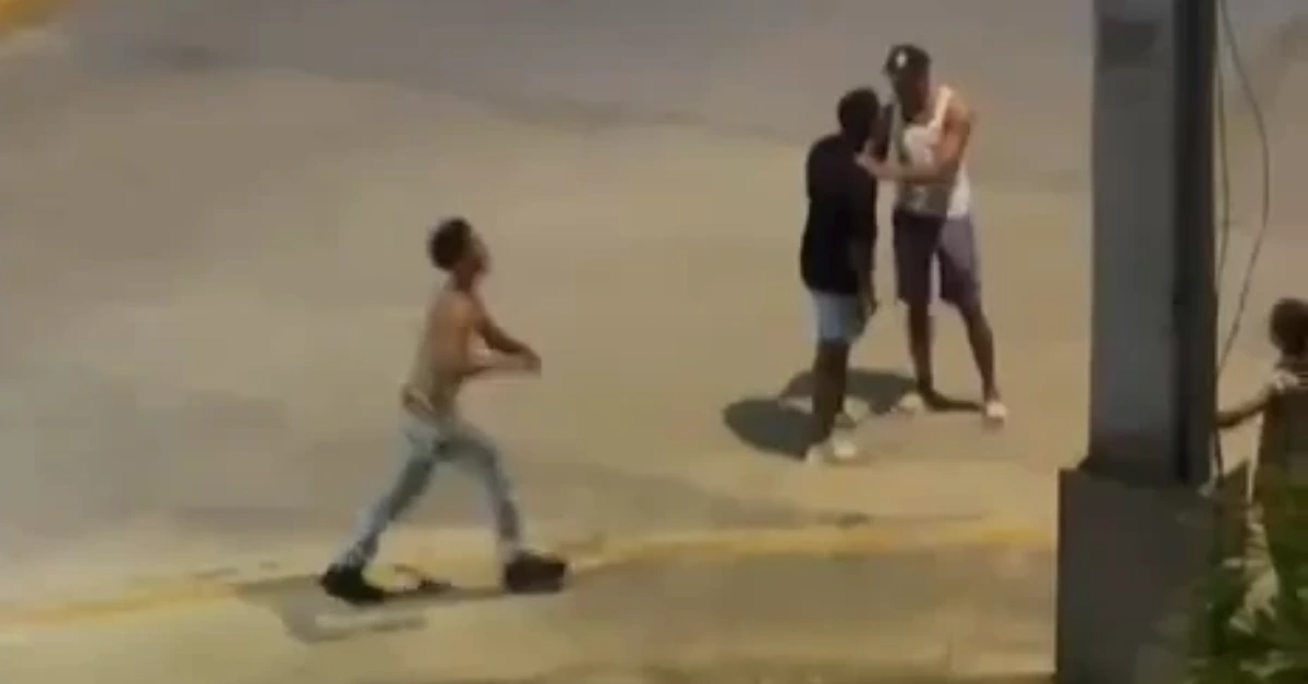 Young boy runs left on a sunny concrete area while two men stand together in the background; a child is near a pillar on the right.