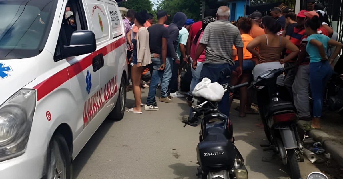 Ambulance parked on a street as a crowd gathers nearby, some people standing by motorcycles and others waiting for assistance.