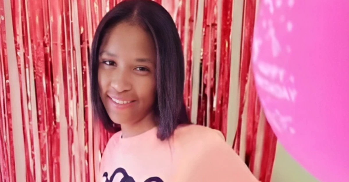 Woman with shoulder-length black hair smiling at the camera, pink shirt, red metallic streamers and a pink balloon in the background.