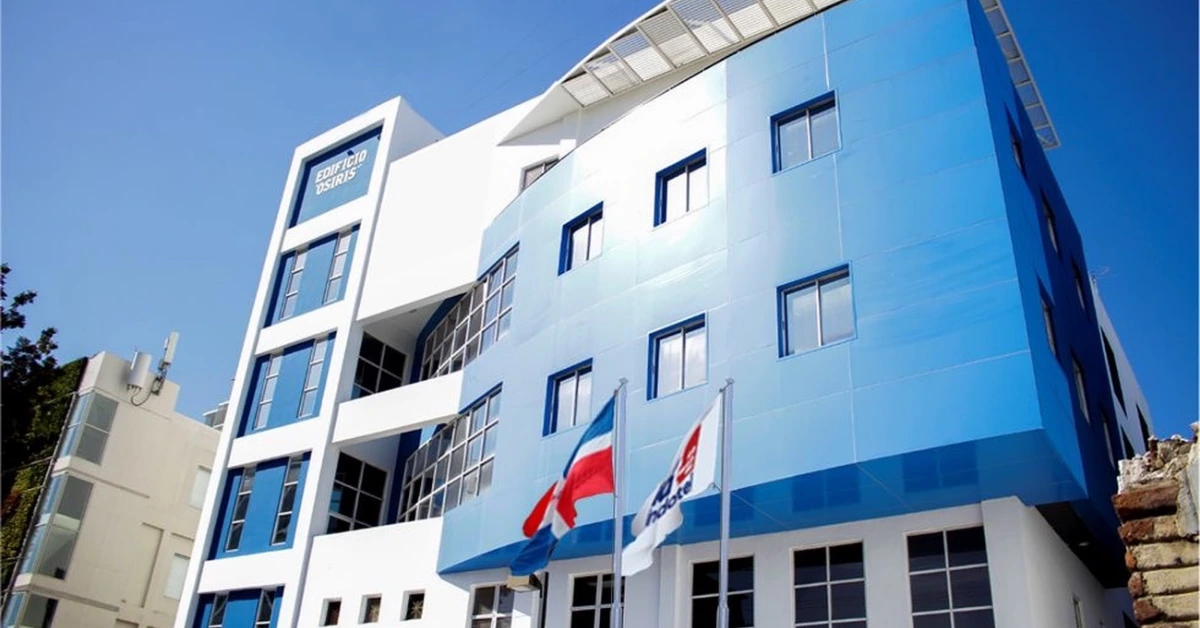 Modern blue-and-white office building with glass windows and two flags at the entrance against a clear blue sky.
