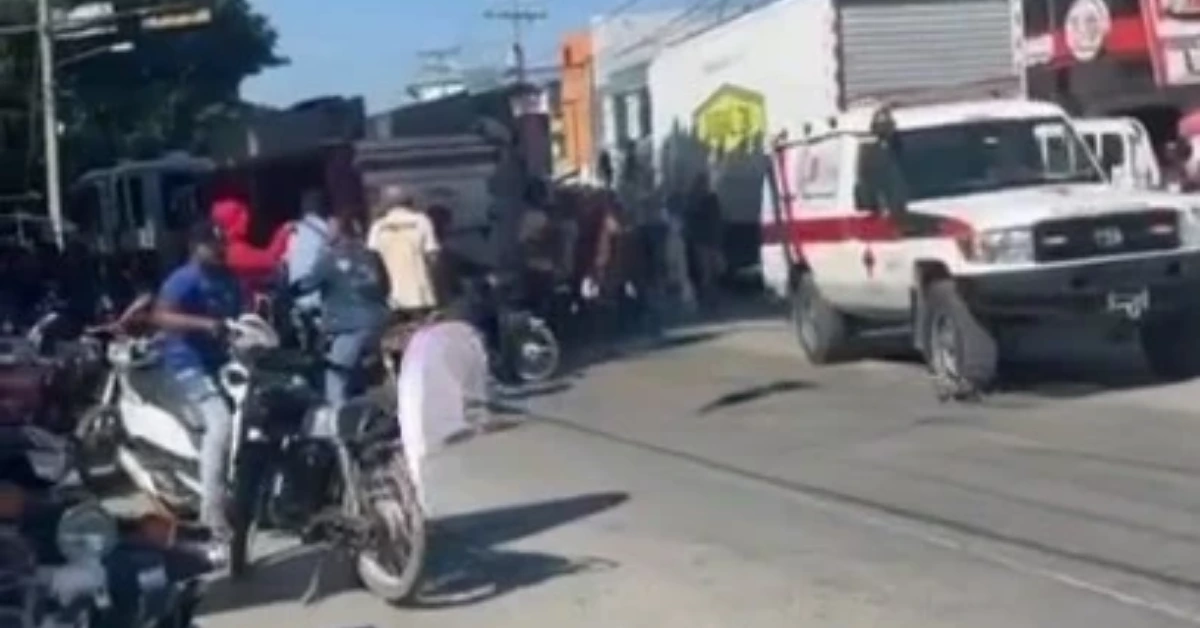 Ambulance on a busy street with pedestrians and motorcycles gathered nearby.