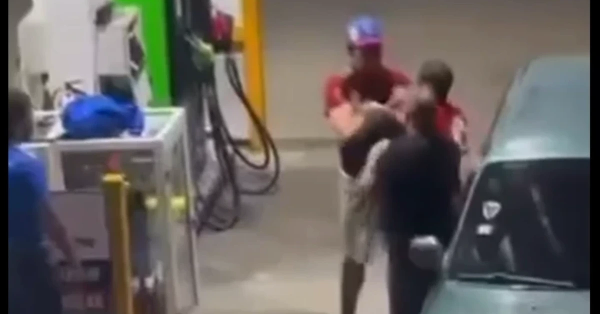 Two people appear to be involved in a confrontation near a gas pump, with a bystander nearby and a car parked beside them.