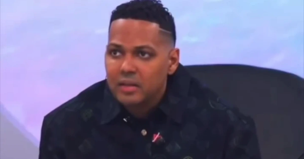 Man on a TV talk-show panel, wearing a black shirt, speaking and looking to the side.