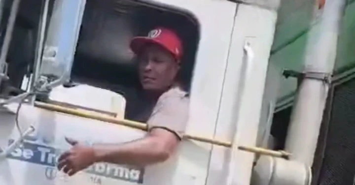 Truck driver wearing a red cap sits in the white cab, looking to the left, with a yellow bar across the window area nearby.