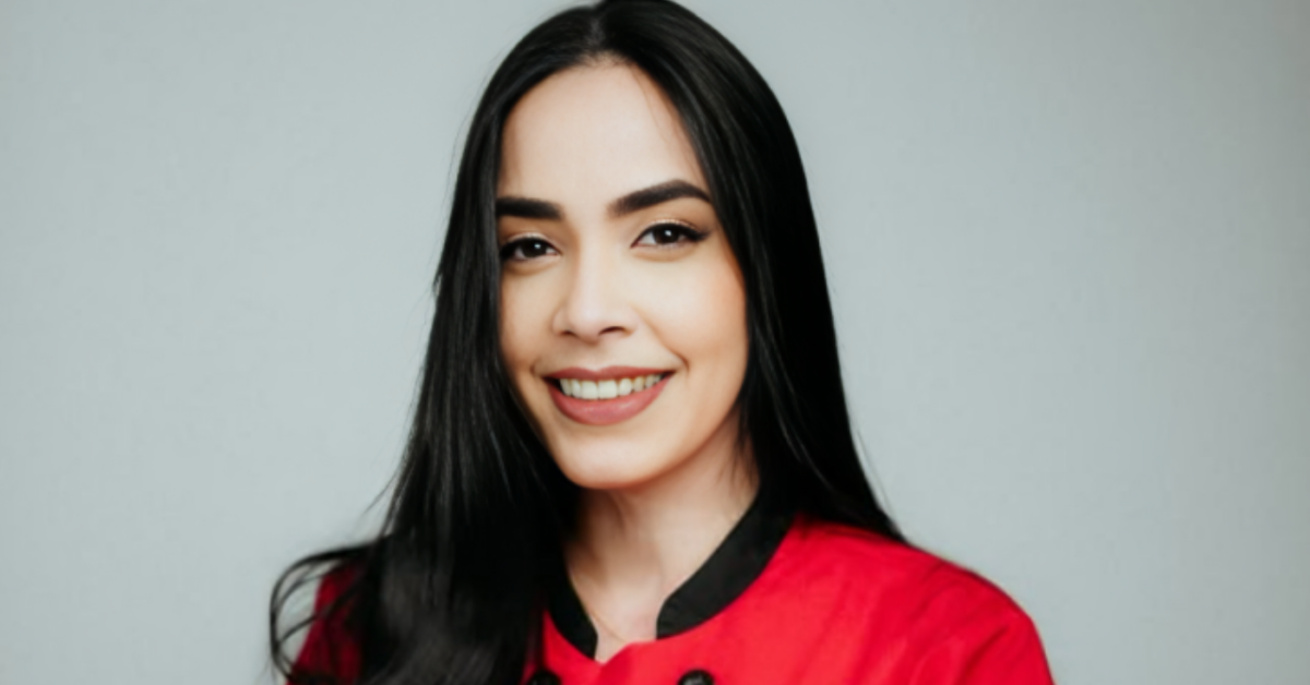 Smiling woman with long black hair in a red uniform against a gray studio background