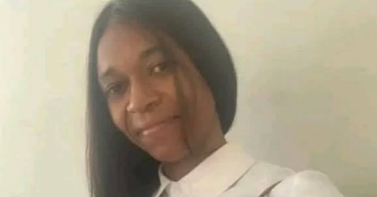 Smiling woman with long black hair in a white collared shirt, posing against a pale wall.