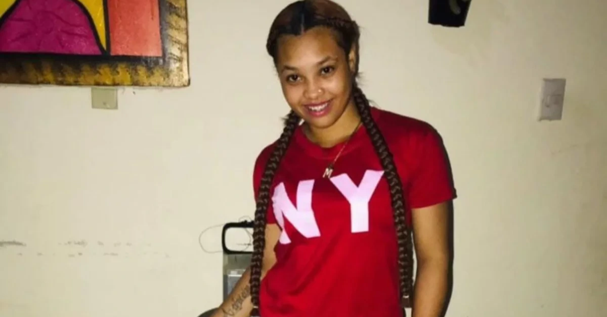Young woman with long braids wearing a red NY T‑shirt, standing indoors and smiling at the camera.