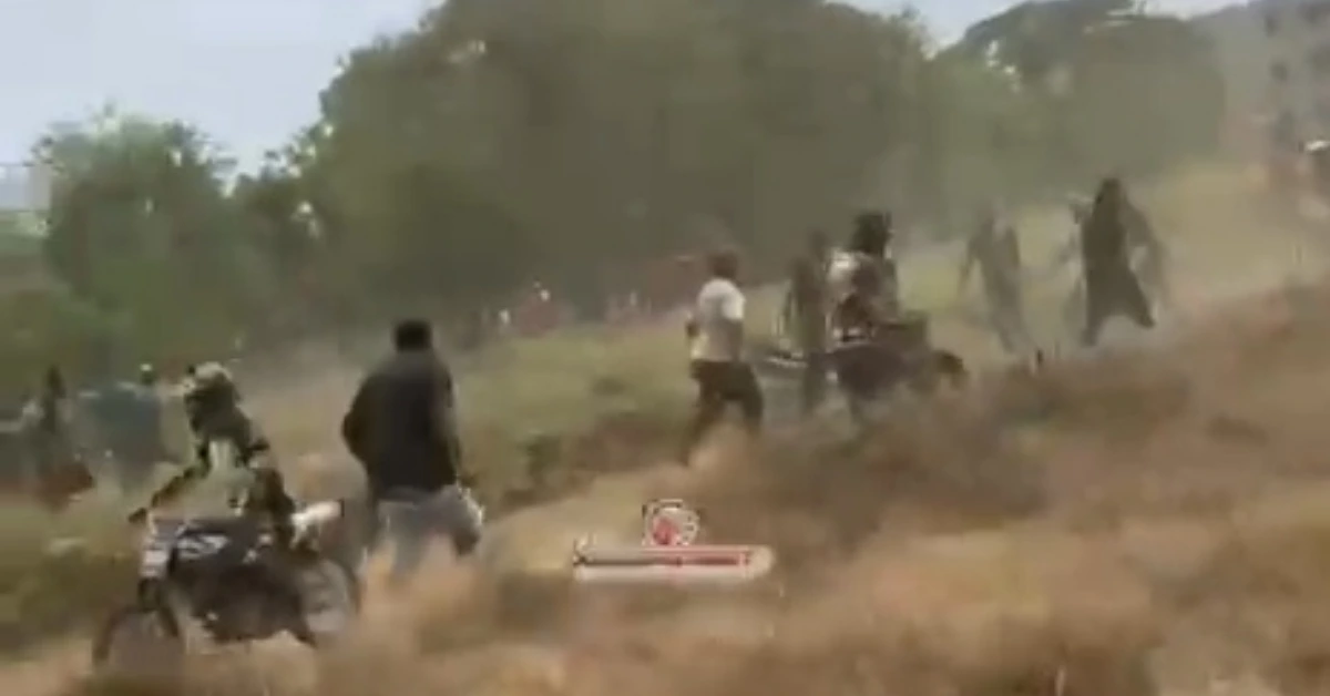 A group of people running across a dusty, open field, some near motorcycles or bikes in the foreground.