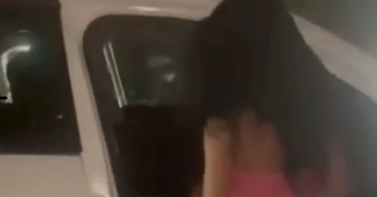Person with long dark hair wearing pink shorts entering a white vehicle at night, seen from behind.