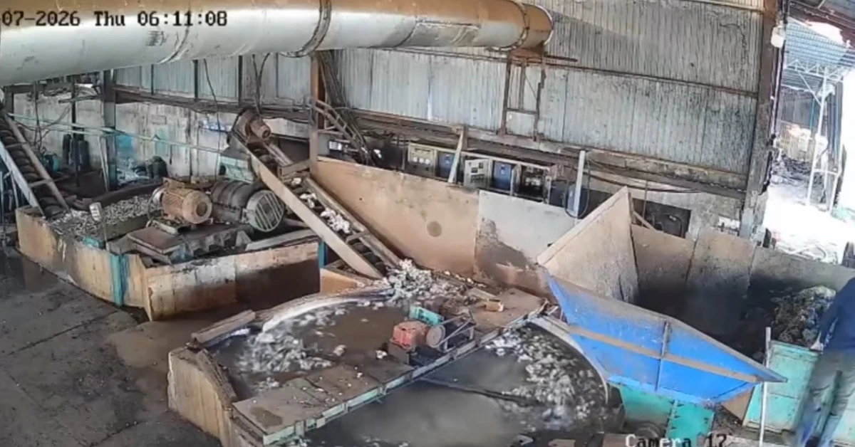 Industrial workshop with rusted machinery, conveyor belts, and a large blue chute amid dirty water and debris on the floor.