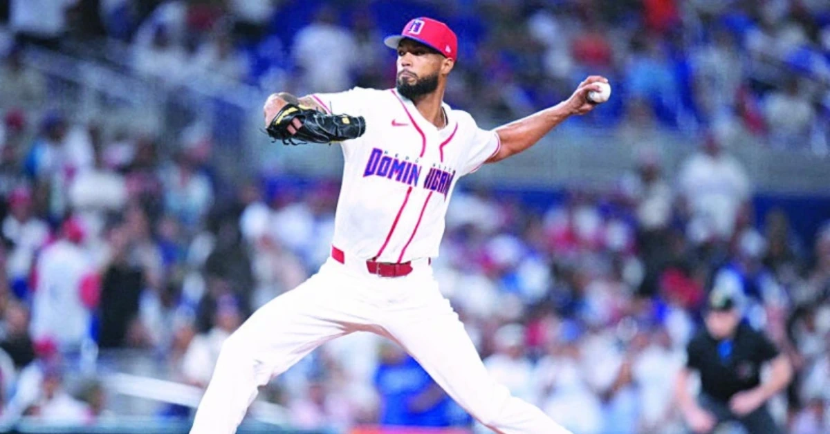 Dominican Republic baseball pitcher in white uniform delivering a pitch on a crowded stadium field, red cap and glove visible.