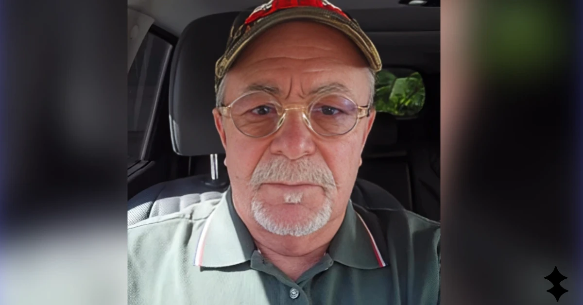 Close-up selfie of a middle-aged man with a gray goatee and glasses wearing a green polo and camo-cap inside a car, looking at the camera.