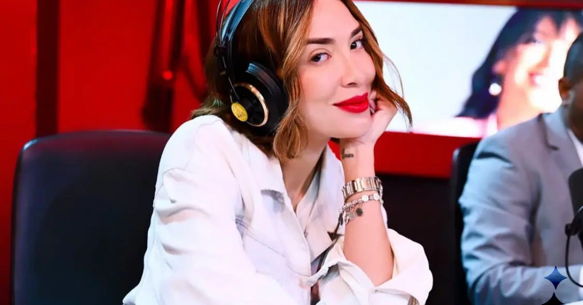 Woman wearing a headset in a studio, resting her chin on her hand as she smiles at the camera in a white shirt.
