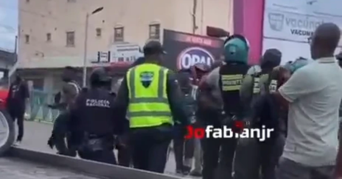 Police and security personnel in high-visibility vests form a barrier on a street with bystanders nearby, during a tense scene.