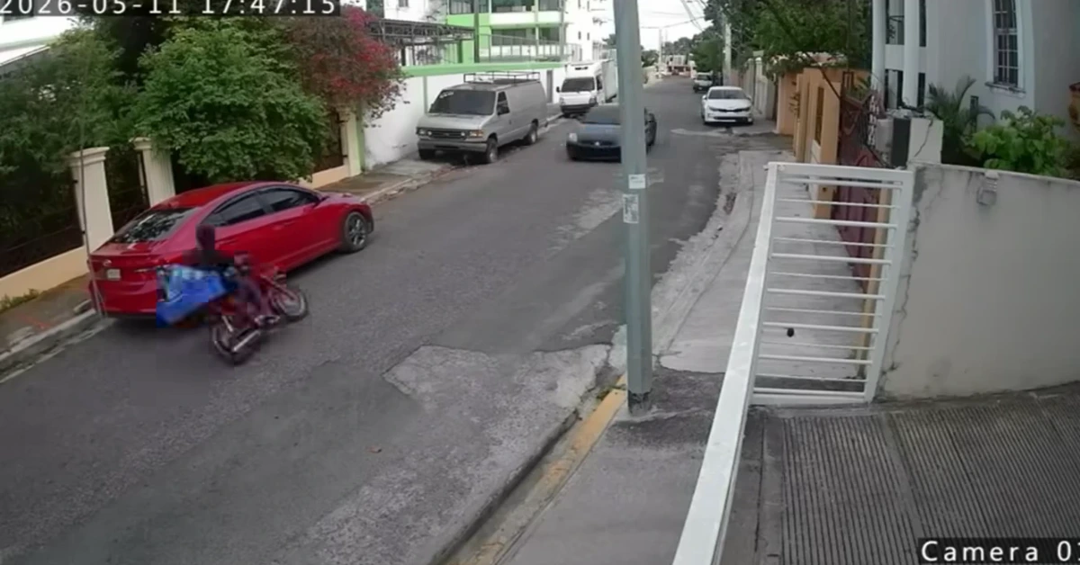Residential street view with a red car and a blue-covered motorcycle on the left, a lamppost in the center, and a white gate on the right; timestamp overlay