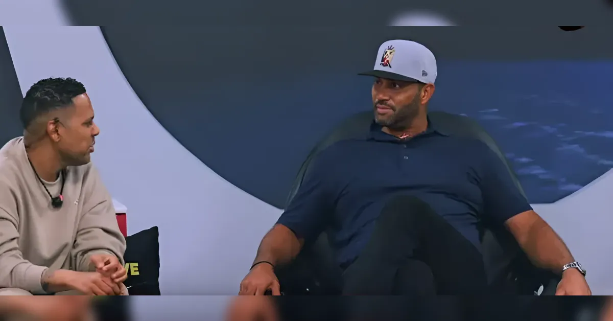 Two men seated on a talk-show set having a conversation on a blue backdrop.
