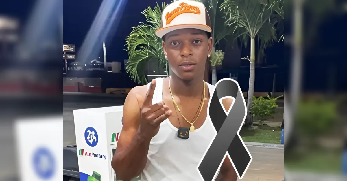Young man in a white tank top and orange cap points at the camera; a gray awareness ribbon overlays his chest at night.