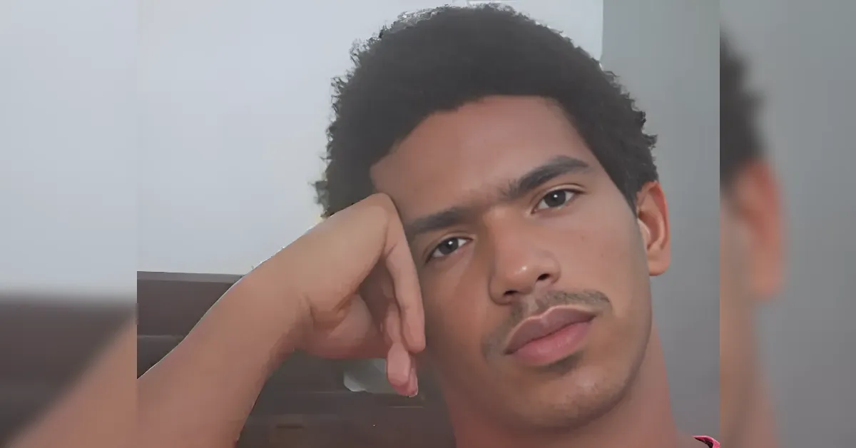 Young man with short dark hair rests his head on his hand and looks into the camera.