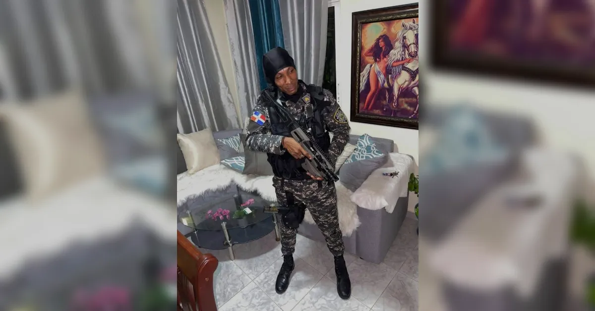 Security officer in camouflage uniform standing indoors, holding a rifle, with a horse painting on the wall behind him.