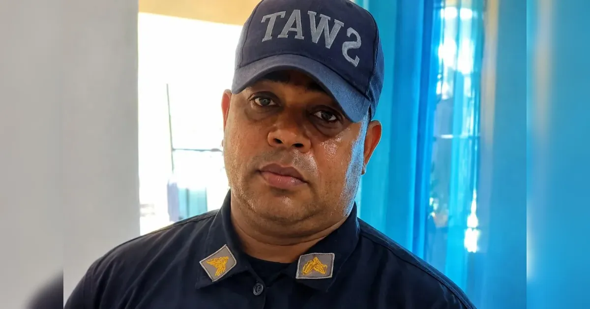 Portrait of a man in a dark uniform wearing a cap that reads 'SWAT' (appearing reversed), looking at the camera with a neutral expression, beads of sweat on his face.