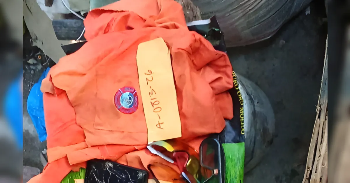 Orange life vest with a handwritten code tag on top of a pile of debris and scattered items.