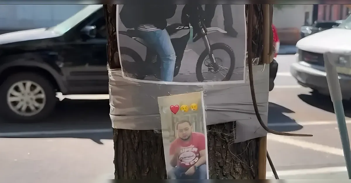 Portrait of a man in a red shirt taped to a tree on a city street, with a heart emoji above the photo.