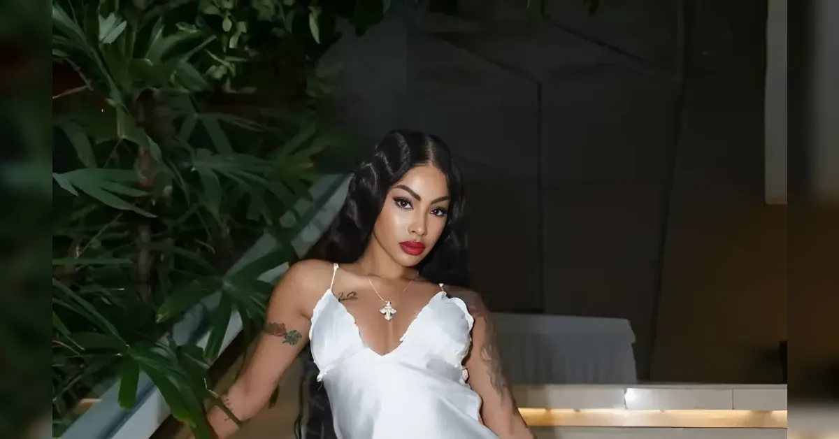 Woman in a white satin slip dress posing beside tropical plants at night on a balcony.