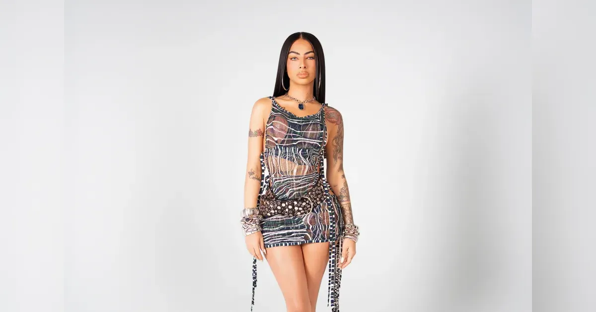 Woman with long black hair wearing a sleeveless animal-print mini dress and a studded belt in a studio setting.