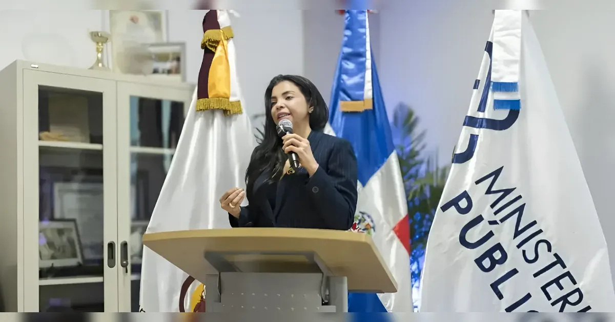 Woman in a dark blazer giving a speech at a podium with a microphone, flanked by flags.