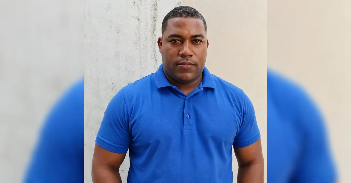 Man wearing a bright blue polo shirt standing against a light textured wall, looking at the camera.