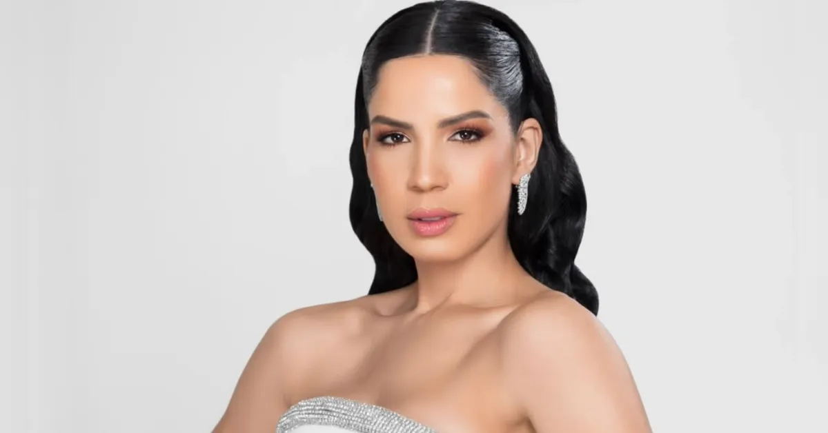 Portrait of a woman with long black hair wearing a sparkling strapless silver gown and diamond earrings against a light background.